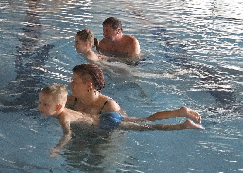 Parent and child splashing feet on the pool edge, both smiling.