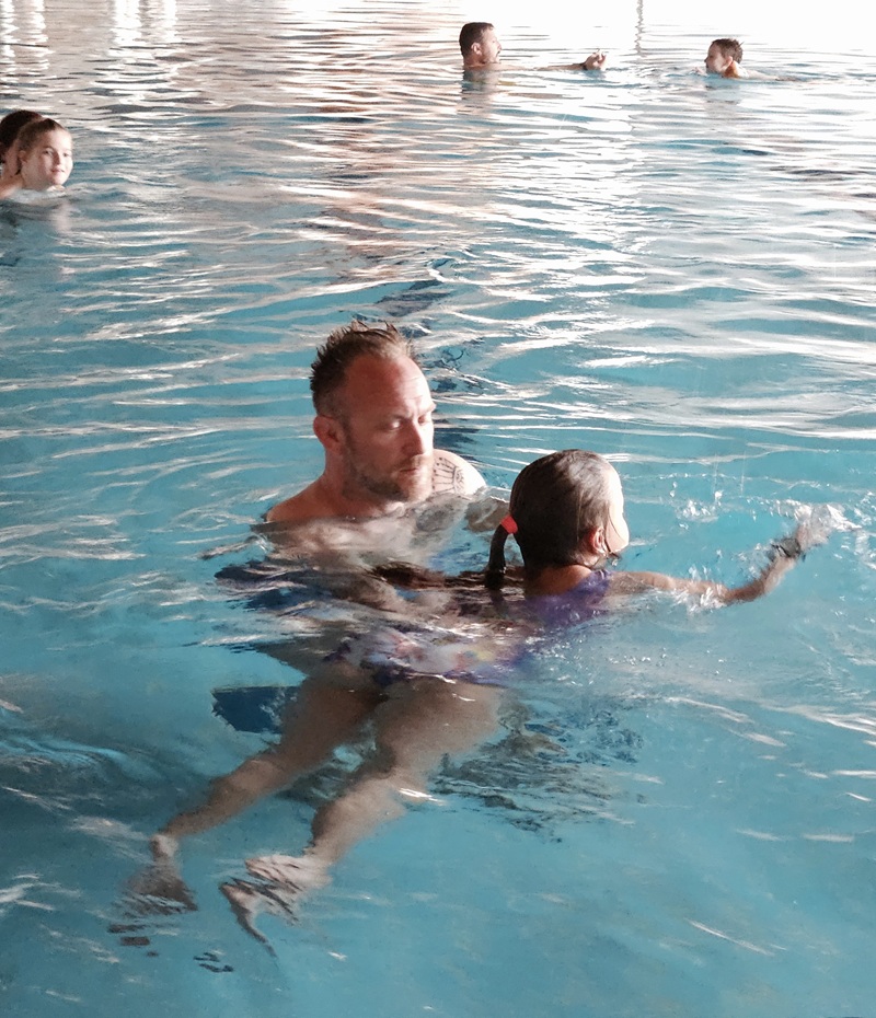 Parent and child splashing feet on the pool edge, both smiling.